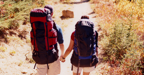 Woman and man with backpacks walk on a path while holding hands
