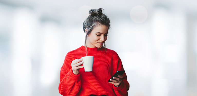 Photo of a woman drinking a coffee and looking at her mobile device 