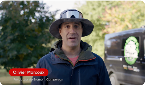Photo of a man speaking to a camera standing in front of a minivan 