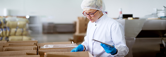 Photo of a woman in a smock checking boxes in a food processing plant