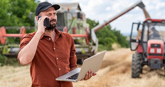 Photo of a man talking on the phone with a laptop in his hand in a field 
