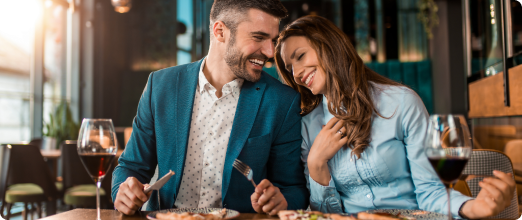 Photo of a man and woman eating at a high-end restaurant with a glass of wine