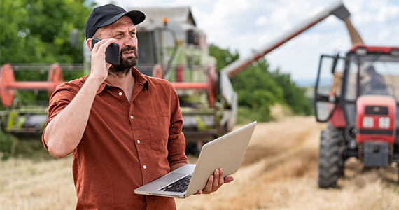 Photo of a man talking on the phone with a laptop in his hand in a field