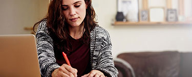 Woman working on her computer and writing with a pen at the same time
