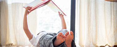 Child lying on his back reading a book