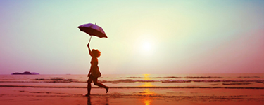 Woman running on the beach at sunset, holding an umbrella