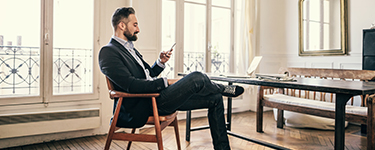 Man in a suit sitting at a desk looks at his phone