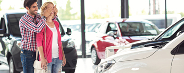 Man hides a woman's eyes in front of a new car