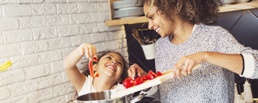 Mother laughing with her young daughter while cooking