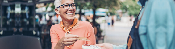 A person sitting at a table outside handing a credit card to pay a waitor