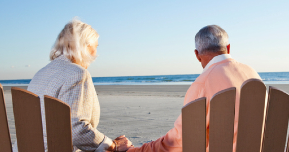 Retired couple holding hands looking at the sea