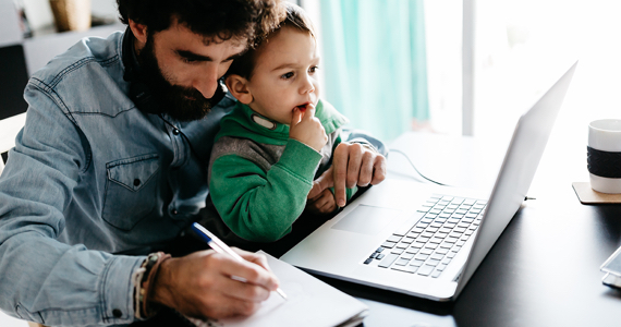Man writing in notebook with child looking at laptop