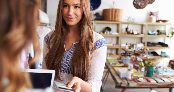 Young woman in a store hands her credit card to a saleswoman