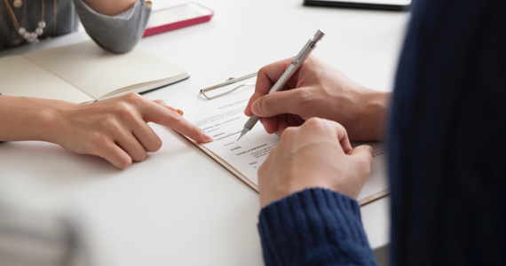 A hand points to a line on a document and another hand holds a pencil