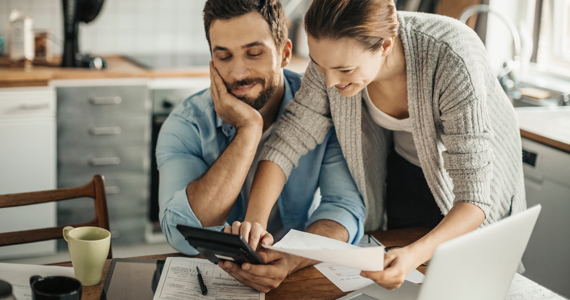 Smiling couple look at documents and point at tablet