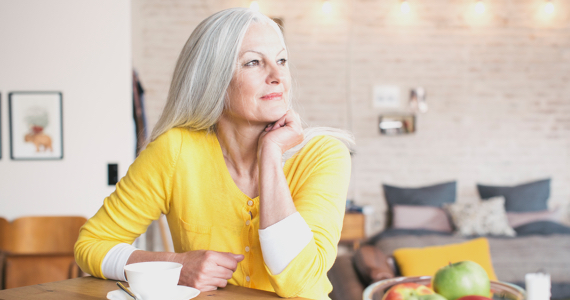Smiling white haired woman is sitting at her kitchen table