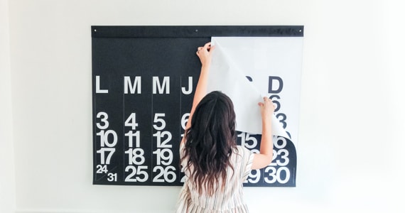 Young woman removes a page from a large calendar hanging on a wall