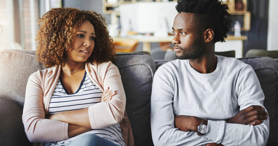 Young woman and young man with arms crossed talk on a couch