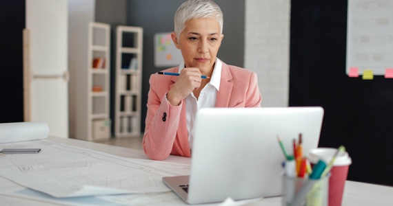 White haired woman at her desk is looking at her computer