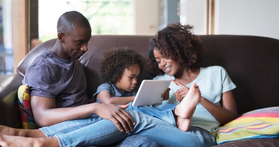Couple and little girl on a couch looking at a tablet