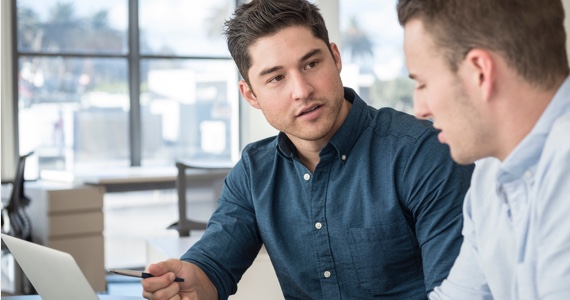 Two men talking in front of a computer