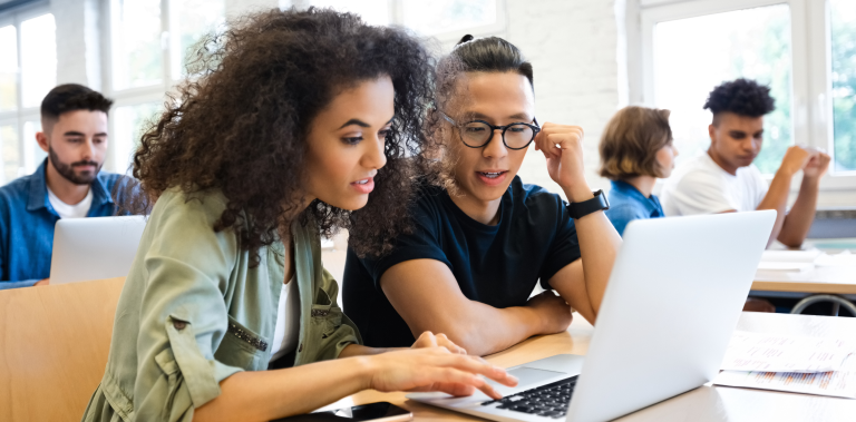Two students sitting in a classroom looking at a laptop screen