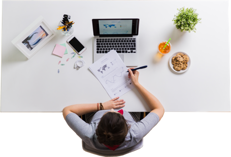 Picture of someone sitting at a desk with a laptop computer in front and the person is writting on a paper sheet