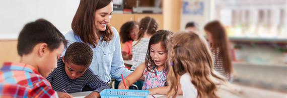 Photo of a woman, smiling and surrounded by children in a school classroom 