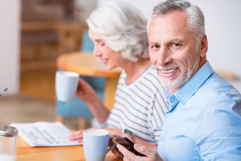 Photo of a retired couple sitting at a table holding cups of coffee 