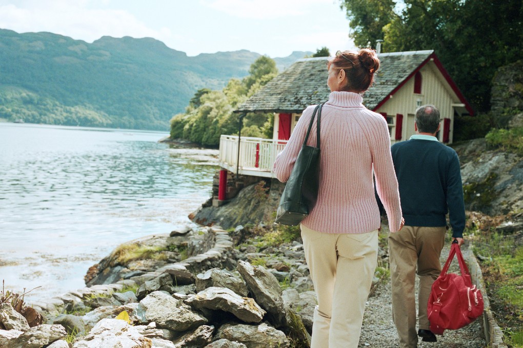 Retired couple walking towards a cottage by the waterside.