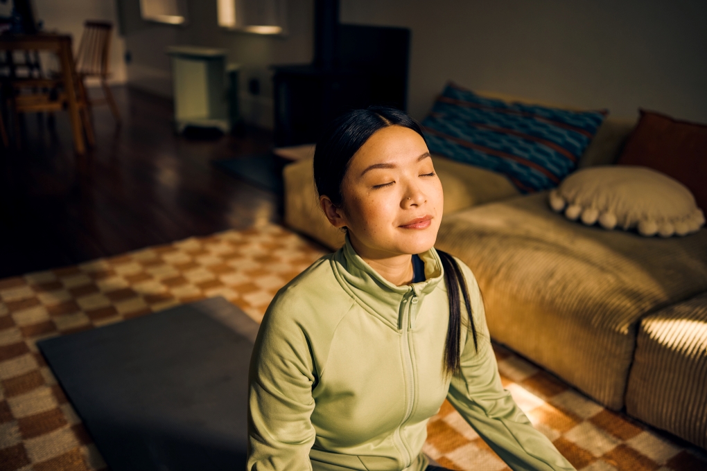 Young woman meditating in living room. 