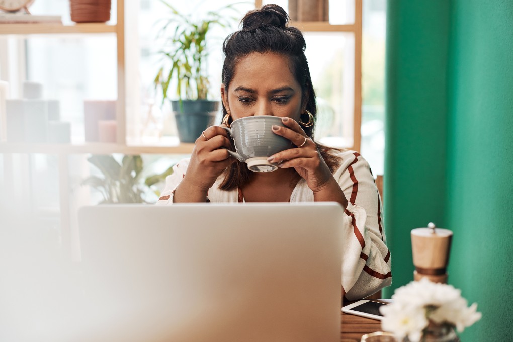 Image of young woman drinking her coffee in front of her computer