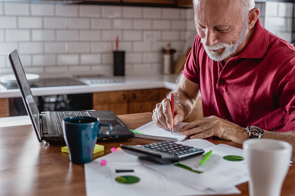 Man with grey hair writing and doing calculations 