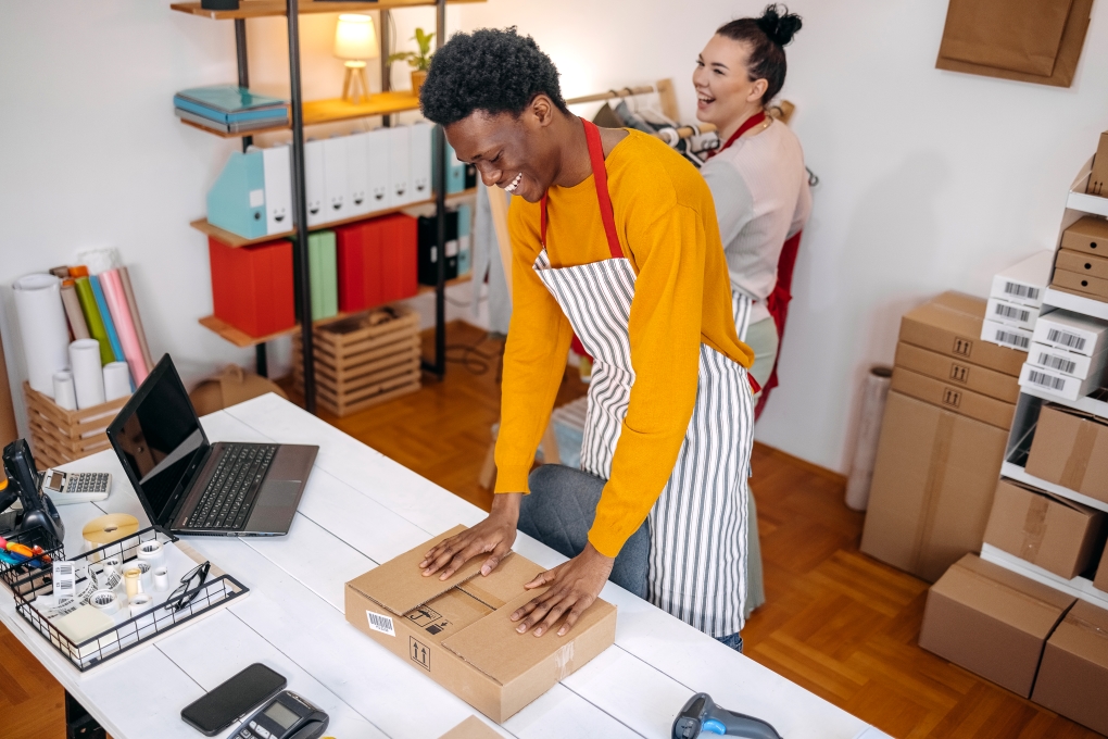 Image for the article on starting your business with a man wrapping up a package while laughing with his collegue
