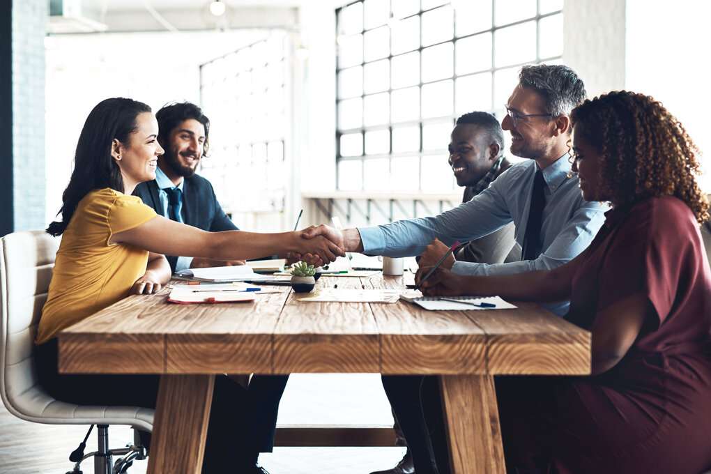 A group of people shaking hands to close a management buyout agreement.