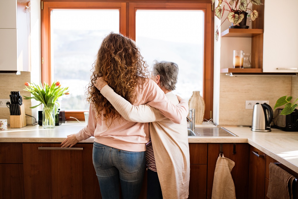 Mother and daughter hugging each other, looking out of the kitchen window