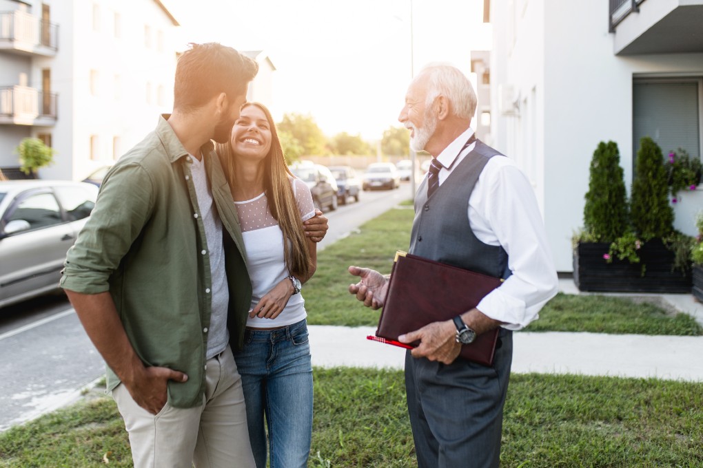 Smiling couple standing in front of a real estate broker 
