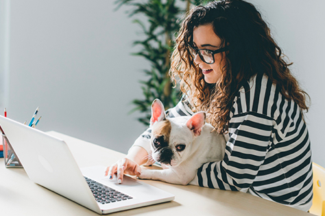Young woman sitting in front of her computer, her dog on her knees 