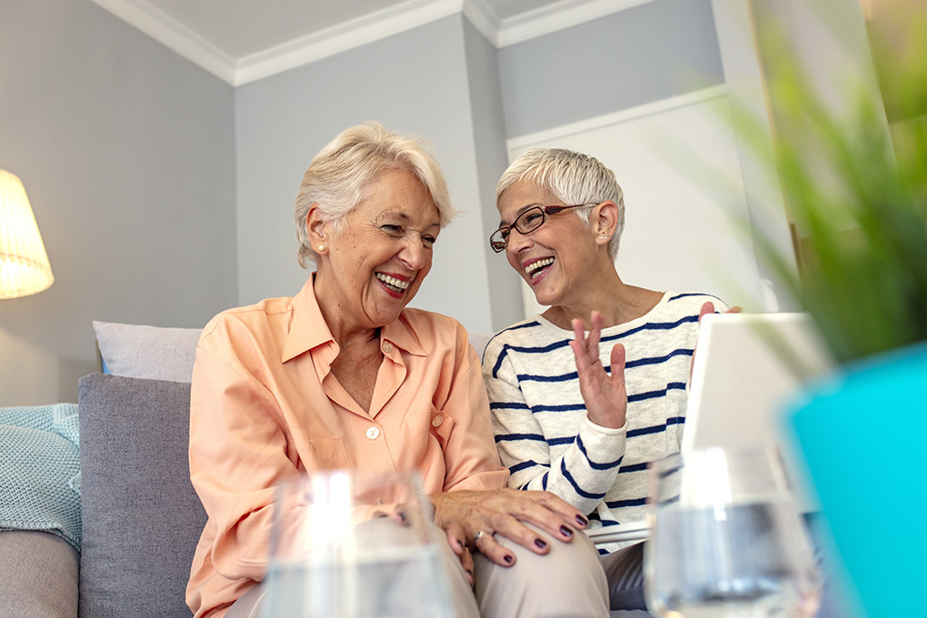 Photo of two retired women sitting on a sofa and laughing together