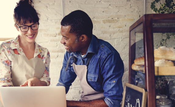 Two people wearing aprons looking at a computer in a workshop