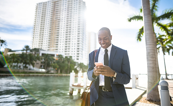 Photo of a man wearing a suit checking his smartphone near a residential tower by the ocean in Florida