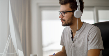 Photo of a man wearing headphones in front of their computer