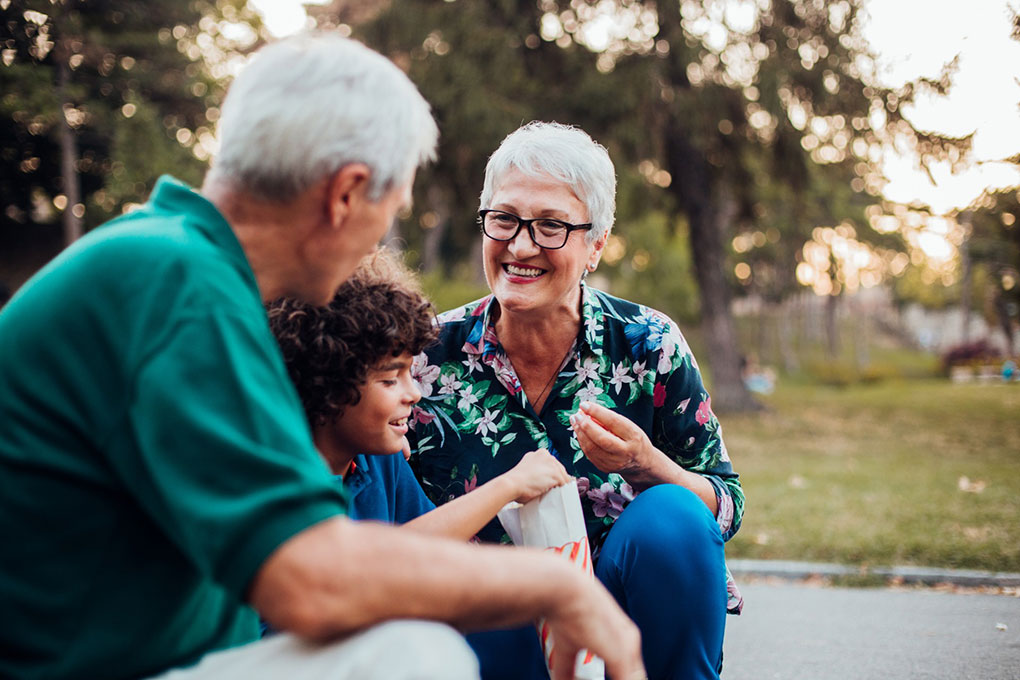 Photo of two smiling grandparents sitting around their grandson