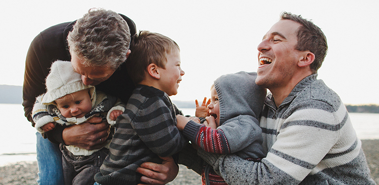 Photo of two men with three young children by the water on a beach