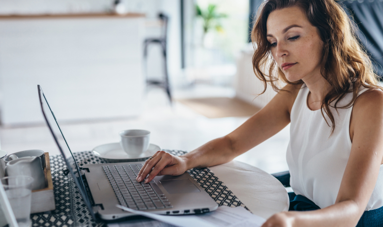 Photo of a woman looking at documents and her laptop in a café
