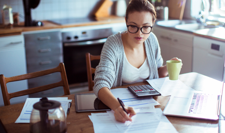 Photo of a woman consulting documents while drinking coffee in her kitchen